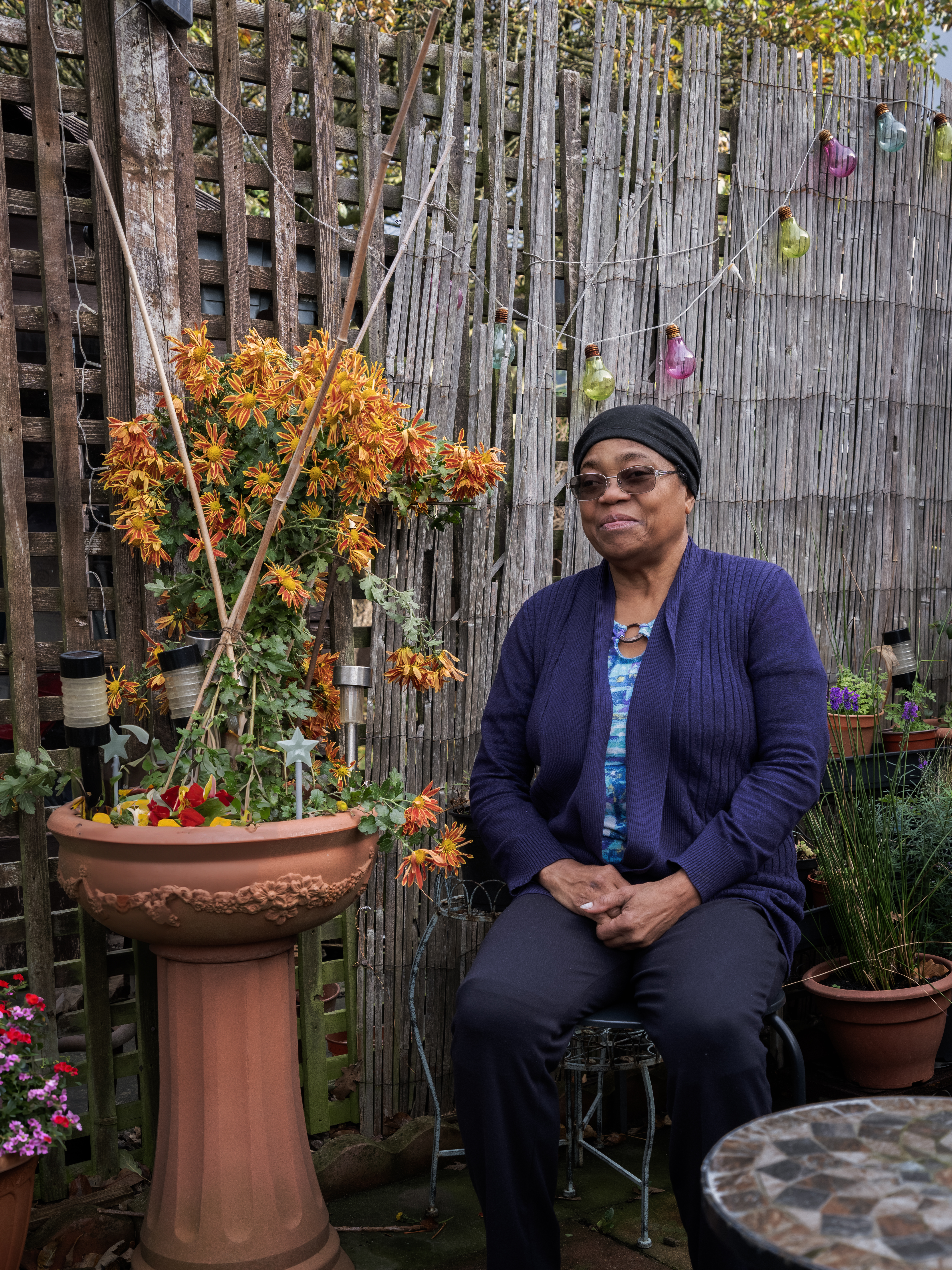 Carol she/her is black Caribbean woman in her 70s. She is photographed in a small section of her back garden which is her favourite place to relax in Gloucestershire. 