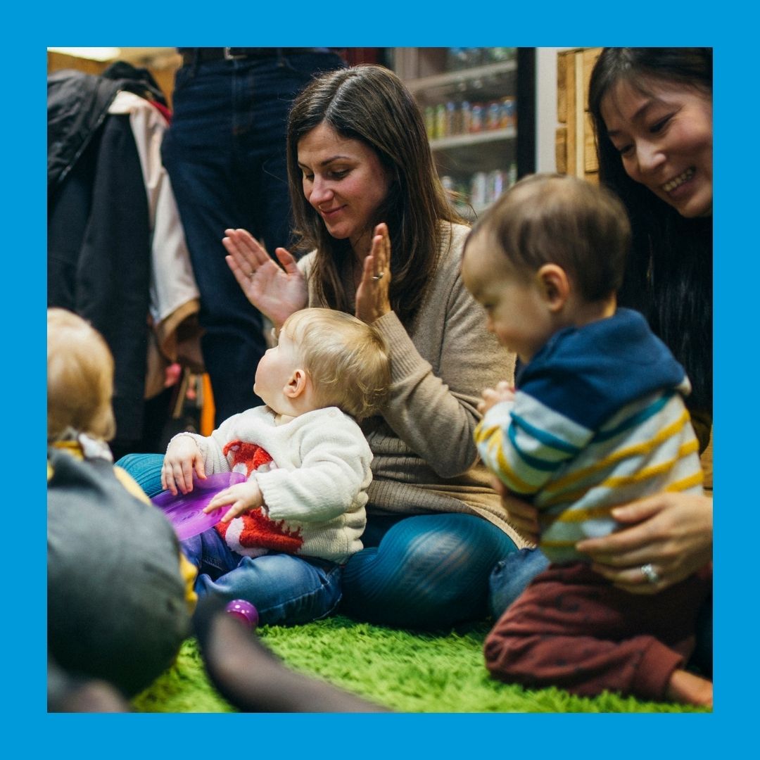 A photo of parents with babies and toddlers in their laps, clapping and smiling