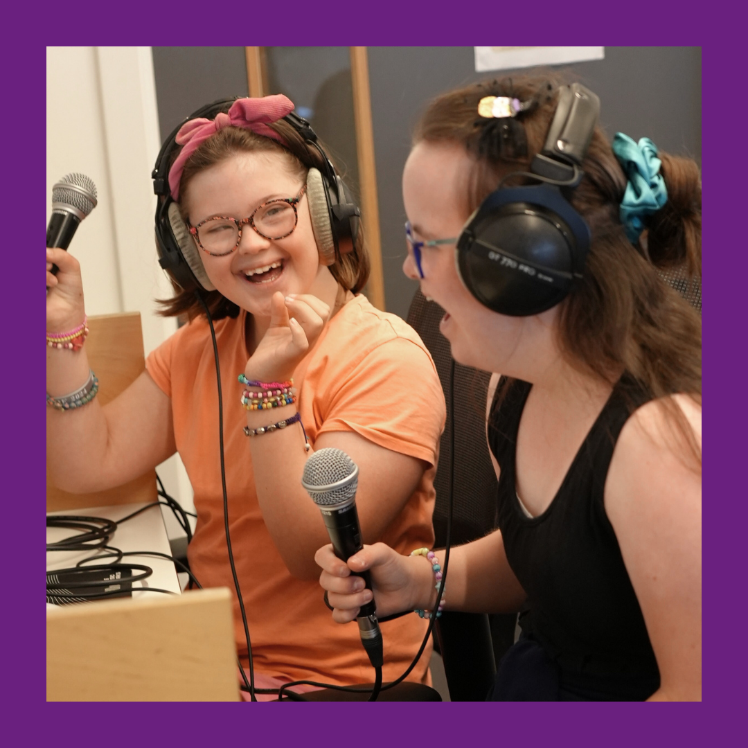Two smiling girls wearing headphones sing into microphones