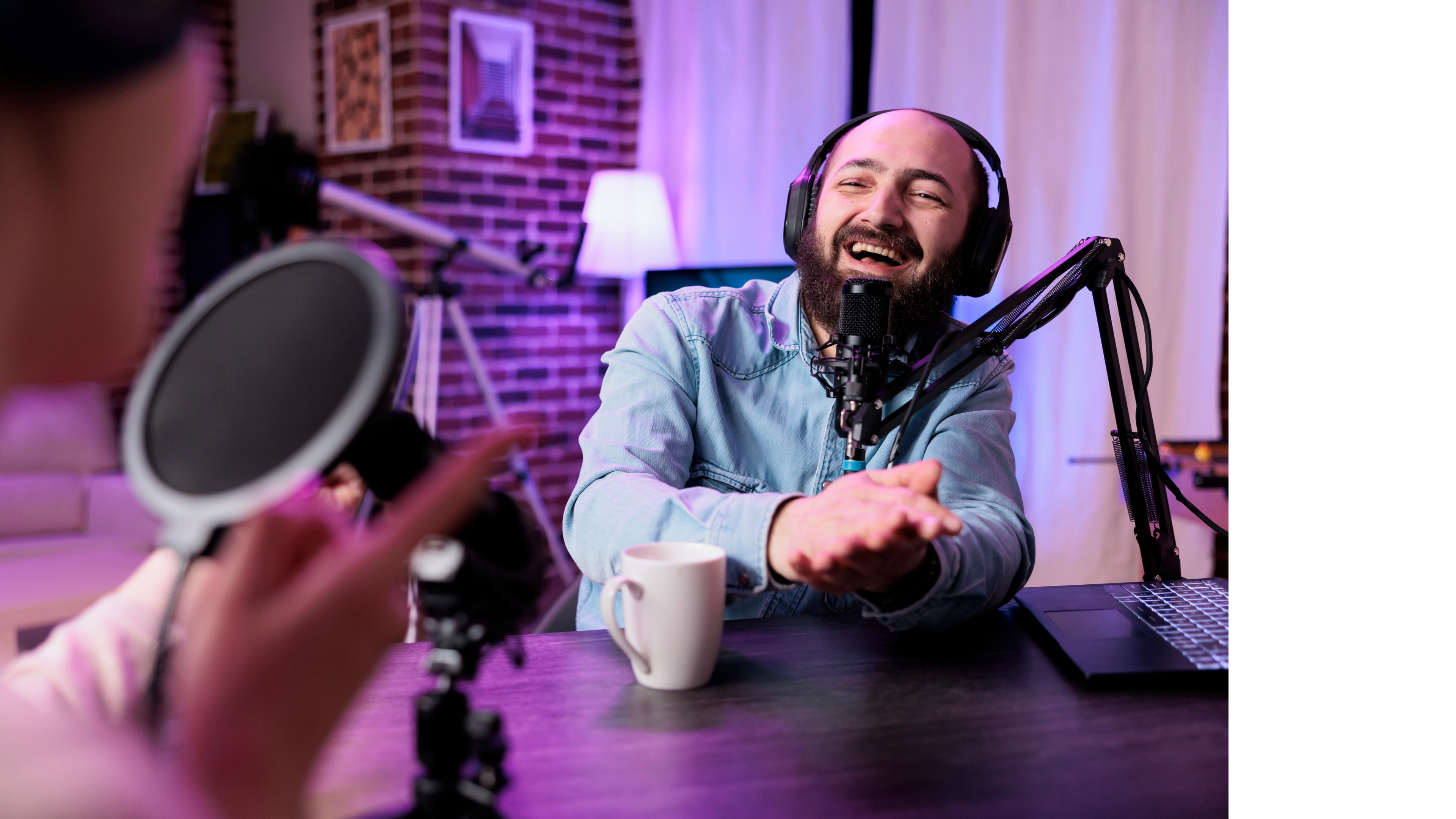 A person wearing headphones talking into a podcasting microphone while smiling.