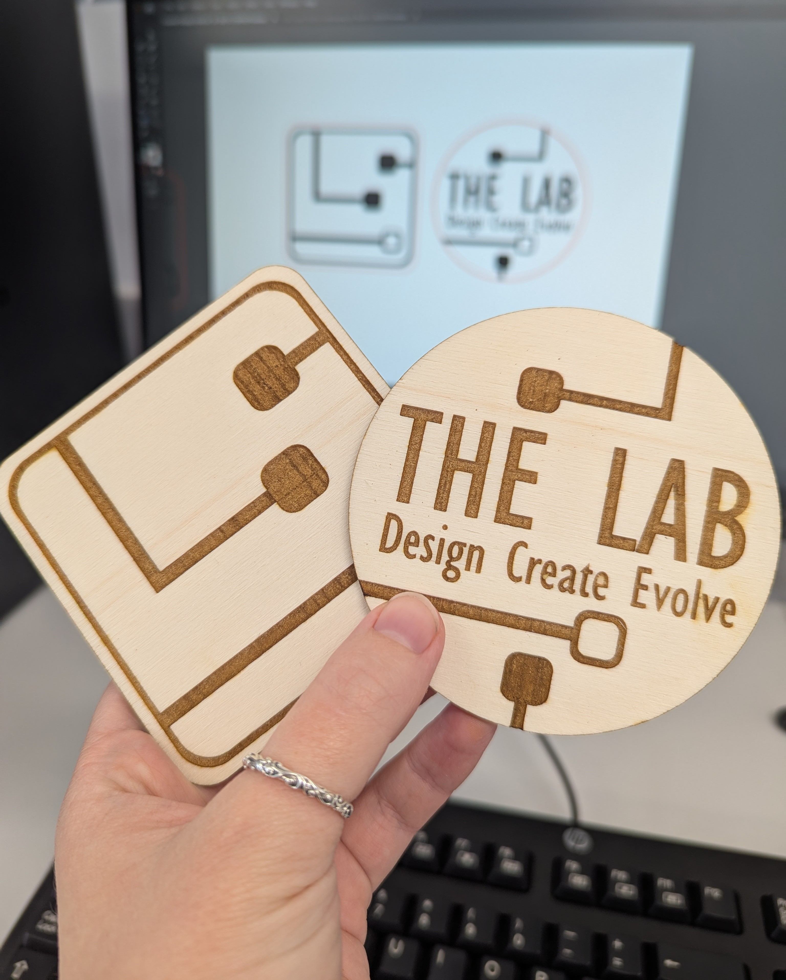 A couple of example coasters in the foreground and digital artwork in the background.