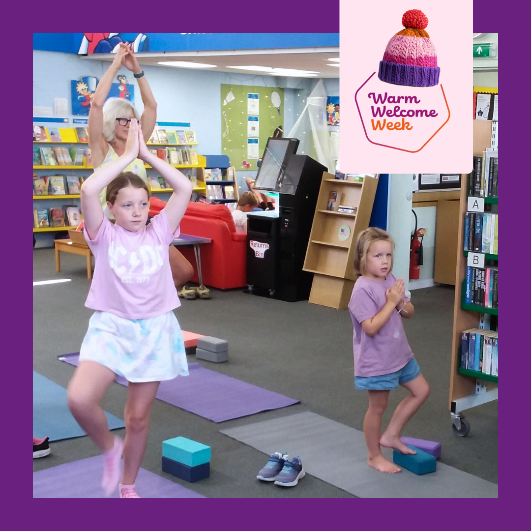 A photo of two girls of varying ages and their grandmother doing a yoga pose on mats in the library