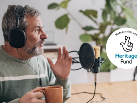 Older man holding hot drink and talking into a microphone for a podcast