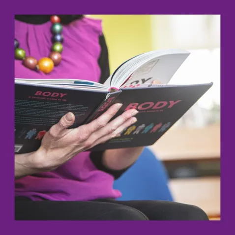 A photo of a woman from the shoulders down holding an open book