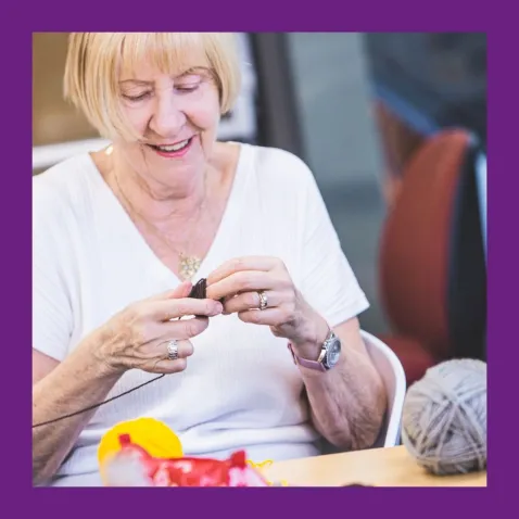 A photo of a woman sitting at a table smiling and winding a ball of yarn