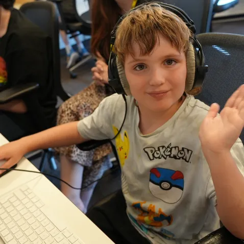 Young boy waving at the camera and wearing headphones