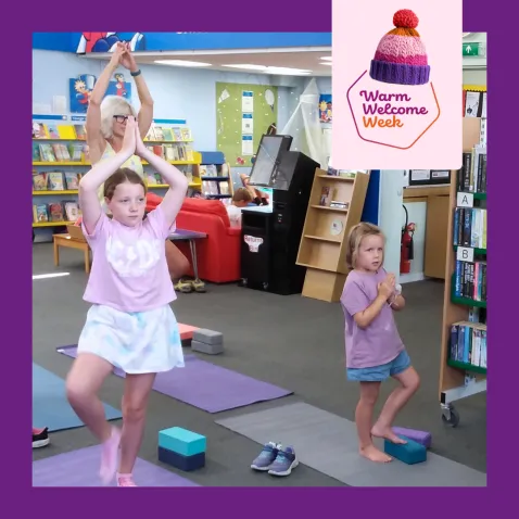 A photo of two girls of varying ages and their grandmother doing a yoga pose on mats in the library