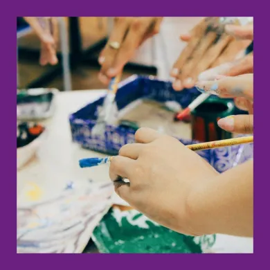 A photo of the hands of several young adults dipping paint brushes into paint