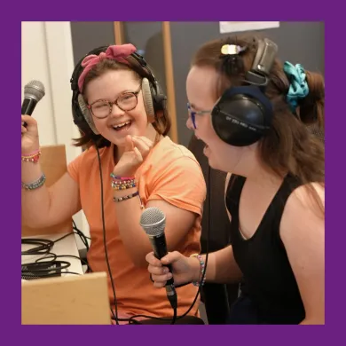 Two smiling girls wearing headphones sing into microphones