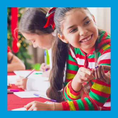 A photo of two children doing a craft with a Christmas tree in the background