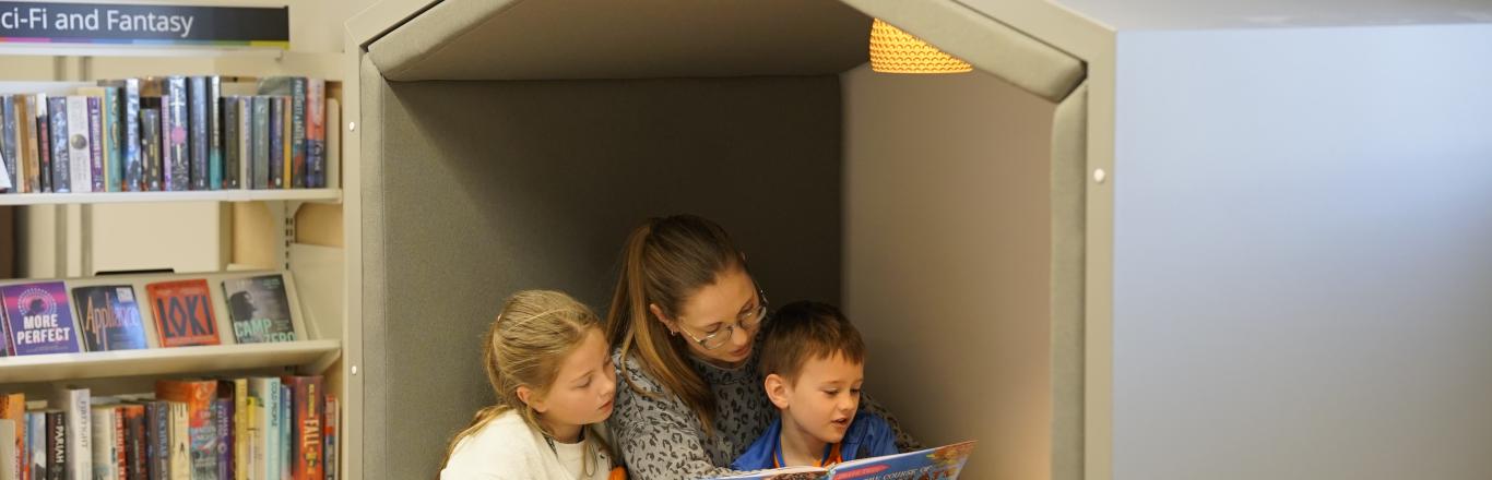 Photo of a woman and two children reading books in a nook in Stroud library