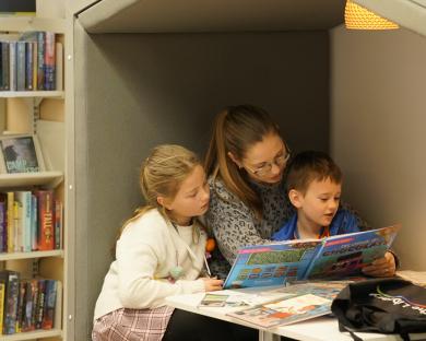 Photo of a woman and two children reading books in a nook in Stroud library