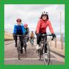 A photo of a line of smiling adults riding bikes along a quiet path.