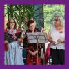 A photo of three women singing in a choir wearing poppy pins with Union Flag bunting hanging in the background.